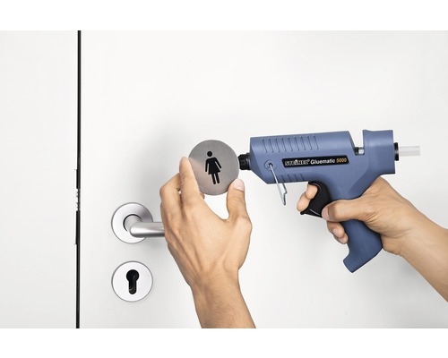 O persoană fixează un simbol pentru femei pe o ușă cu un pistol de lipit.