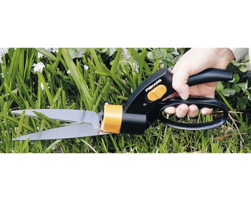 O persoană taie iarbă cu o foarfecă de iarbă Fiskars.