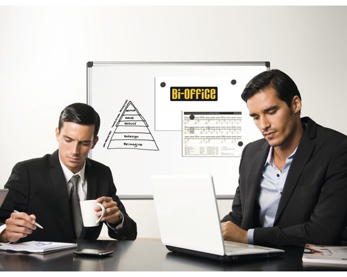 Doi bărbați stau la o masă cu un laptop în fața unei prezentări pe tablă într-un birou.