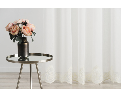 Perdea decorativă, transparentă, cu motiv floral în partea de jos și măsuță laterală cu vază de flori