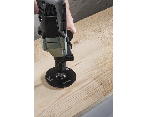 O bormașină cu disc abraziv prelucrează o scândură de lemn.