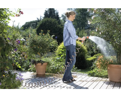 Femeie udând plante cu un furtun de grădină în grădină.