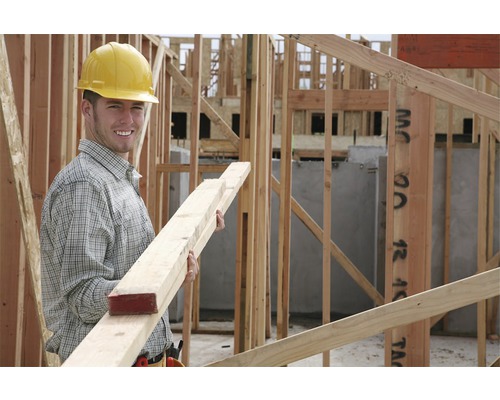 Un muncitor în construcții cu cască de protecție ține scânduri de lemn pe un șantier.