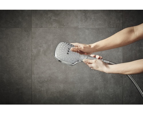 Cap de duș cu furtun de duș în mâini în fața plăcilor de perete