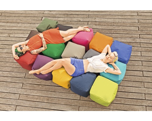 Două femei se relaxează pe o grămadă de perne pătrate în aer liber.