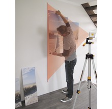 Un bărbat aliniază o imagine pe un perete cu o nivelă laser cu linii.