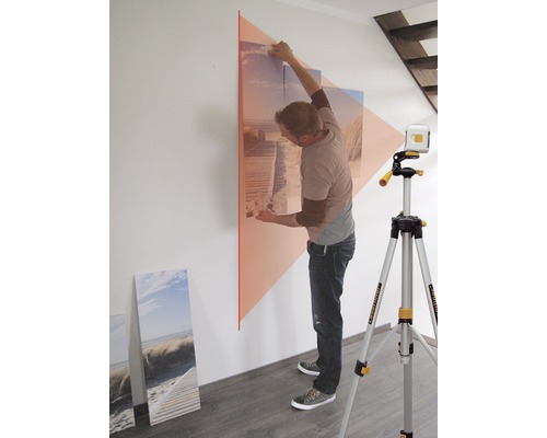 Un bărbat aliniază o imagine pe un perete cu o nivelă laser cu linii.