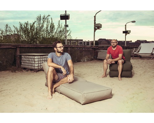 Doi bărbați se relaxează pe o suprafață nisipoasă cu mobilier de lounge.