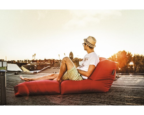 Bărbat cu pălărie se relaxează pe un sac de fasole roșu cu suport pentru picioare pe un acoperiș