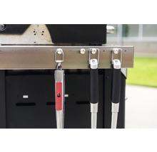 Clește de grătar și ustensile de grătar atârnate de un grătar