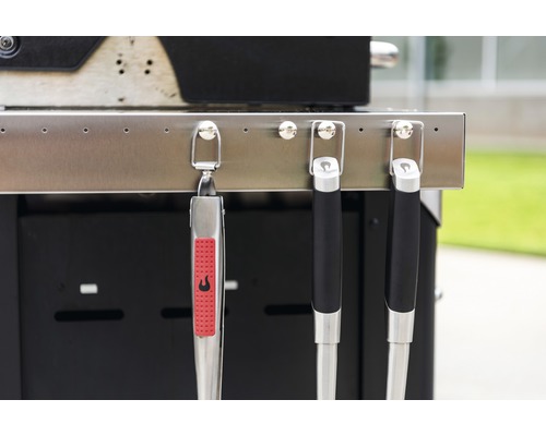 Clește de grătar și ustensile de grătar atârnate de un grătar