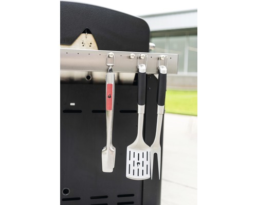 Unelte pentru grătar atașate la un grătar, inclusiv clești, spatulă și furculiță