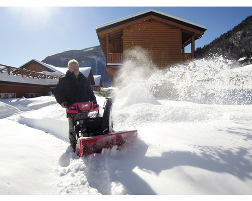 O persoană folosește o freză de zăpadă pentru a curăța zăpada din fața caselor de lemn.