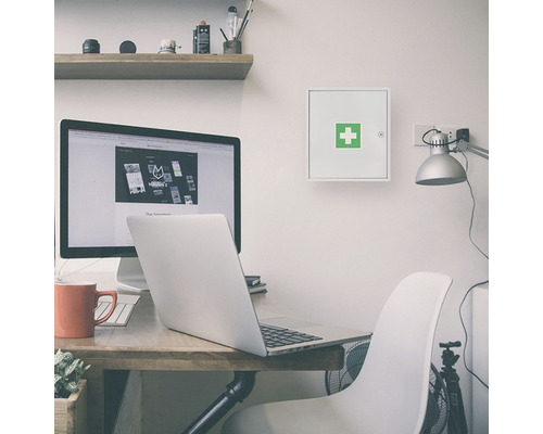 Birou cu masă de scris, computer și o trusă de prim ajutor montată pe perete.