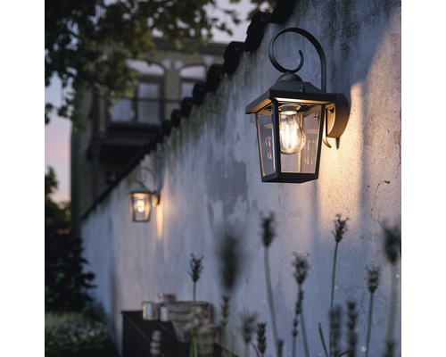 Lămpi de perete exterioare pe un perete iluminează o zonă de grădină.