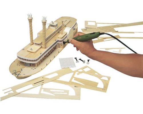 Scenă de modelism cu un vapor cu zbaturi din lemn, diverse piese din lemn și un instrument multifuncțional într-o mână.