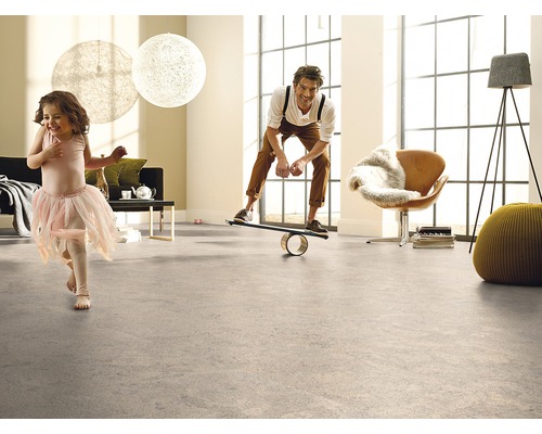 Cameră de zi luminoasă cu pardoseală, în care un bărbat stă pe o placă de echilibru și un copil se plimbă