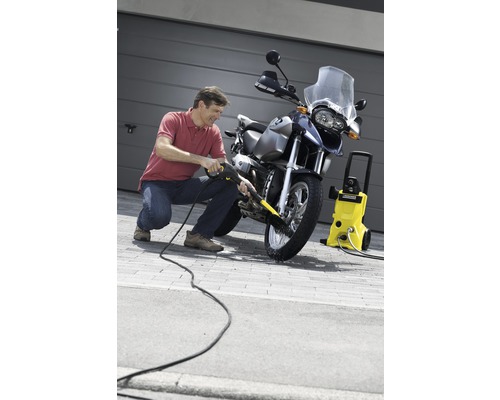 Bărbat curăță motocicletă cu un curățător cu presiune înaltă în fața garajului