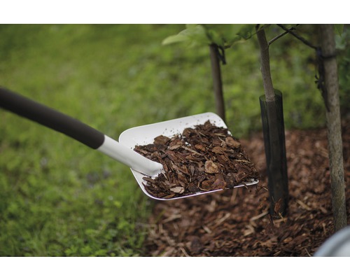 O lopată plină cu mulci de scoarță este împrăștiată în jurul unui copac.