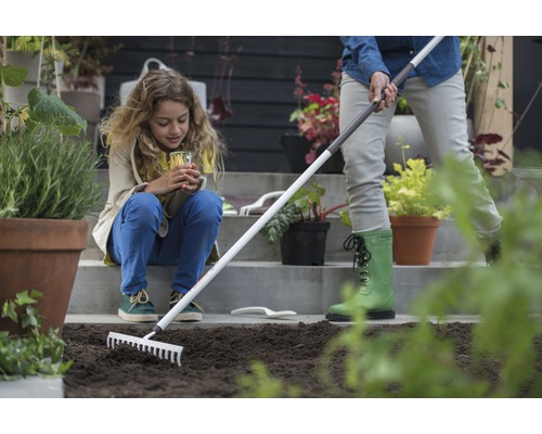 Scenă de grădinărit cu o femeie care pregătește pământul cu o greblă, în timp ce un copil se uită