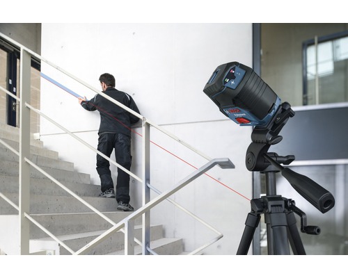 Șantier cu laser liniar pe trepied și artizan pe scări