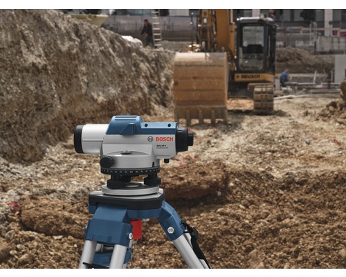 Șantier cu nivelă optică pe trepied și excavator în fundal