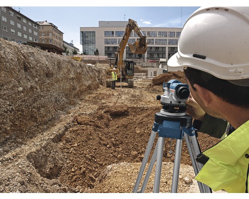 Muncitor în construcții lucrând cu un nivel optic pe un șantier