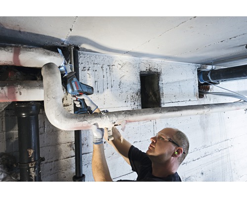 Un bărbat taie o țeavă într-un subsol cu un fierăstrău electric.