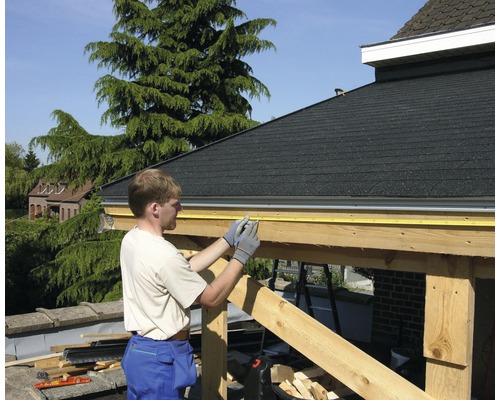 Un bărbat măsoară o construcție din lemn cu o ruletă.