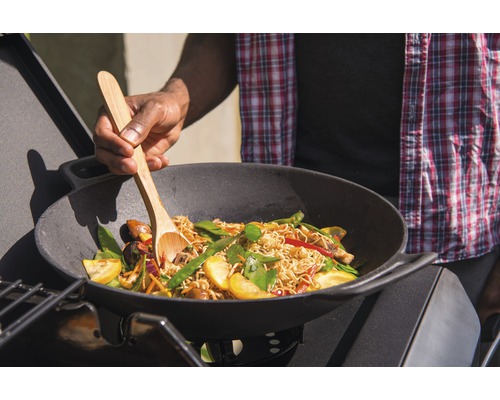 Bărbat gătește tăiței cu legume într-un wok pe un grătar