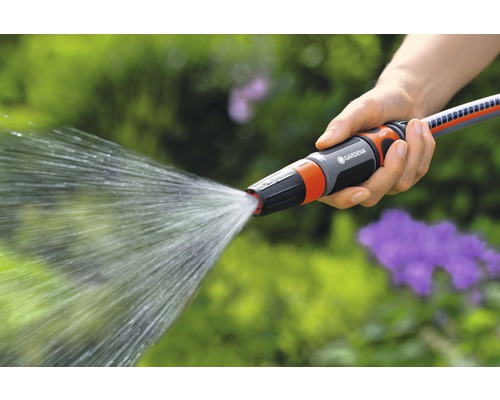 O persoană ține un furtun de grădină cu duză de pulverizare în mână, din care iese apă.