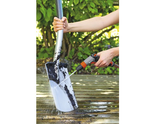 O persoană curăță o lopată cu un jet de apă pe o suprafață de lemn.