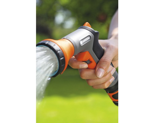 O mână ține un duș de grădină Gardena din care curge apă.