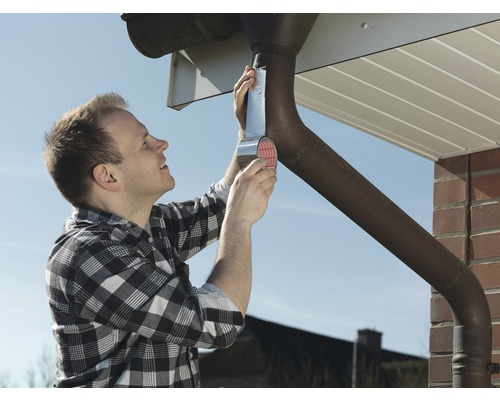 Un bărbat repară o jgheabă cu bandă de etanșare.