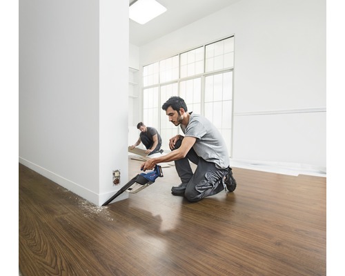 Doi meseriași instalează parchet laminat cu un ferăstrău vertical într-o cameră luminoasă.