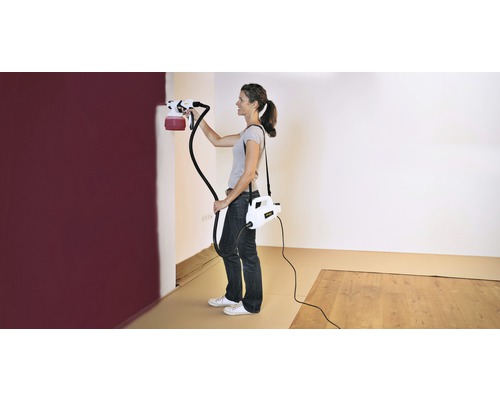 Femeie care pictează un perete cu un sistem de pulverizare a vopselei într-o cameră