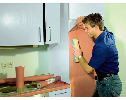 Un bărbat aplică folie pentru mobilă într-o bucătărie