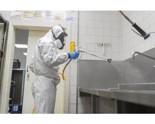 O persoană în echipament de protecție pulverizează o suprafață cu un pulverizator