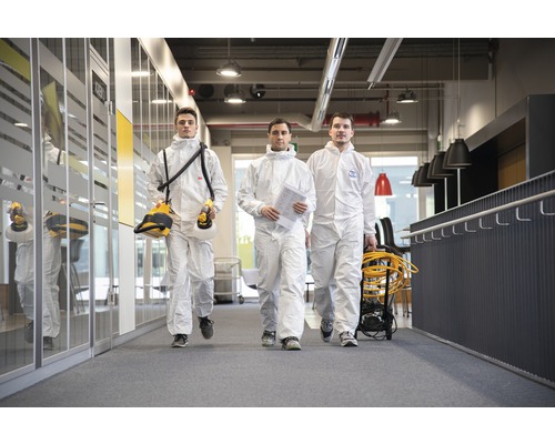 Trei persoane în costume de protecție merg într-un birou.