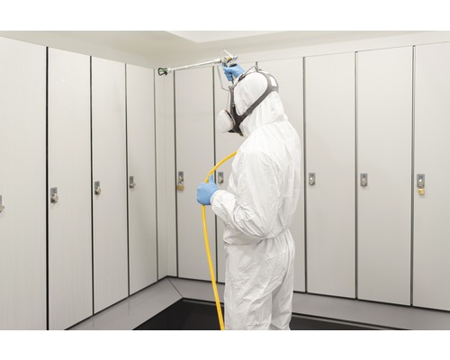 Bărbat în costum de protecție dezinfectează dulapuri cu pulverizator