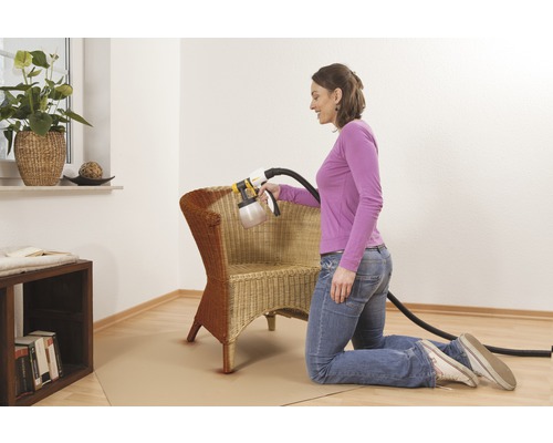 Femeie care lăcuiește un scaun din răchită cu un sistem de pulverizare a vopselei