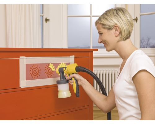 Femeie folosind pistol de pulverizare vopsea pe comoda cu șabloane de soare