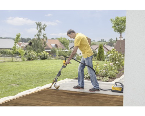 Un bărbat tratează o terasă din lemn cu un sistem de pulverizare a vopselei Wagner în grădină.