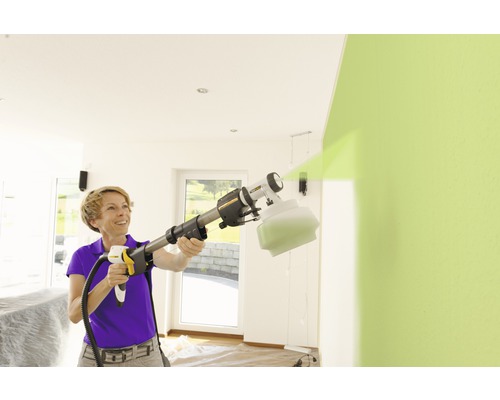 Femeie folosind un sistem de pulverizare a vopselei pentru a vopsi un perete în interior.