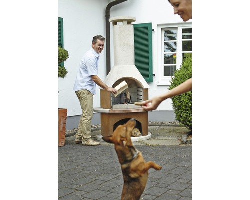 Scenă cu un bărbat care pune lemne într-un grătar de grădină, în timp ce o femeie dă o gustare unui câine.