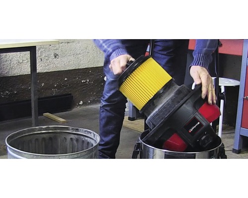 O persoană golește filtrul unui aspirator de cenușă într-o găleată metalică.