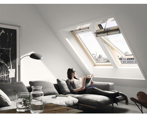 Fereastră de mansardă VELUX cu acționare electrică GGLCK02306621 Cameră luminoasă de mansardă cu ferestre de mansardă și o femeie întinsă pe o canapea citind.