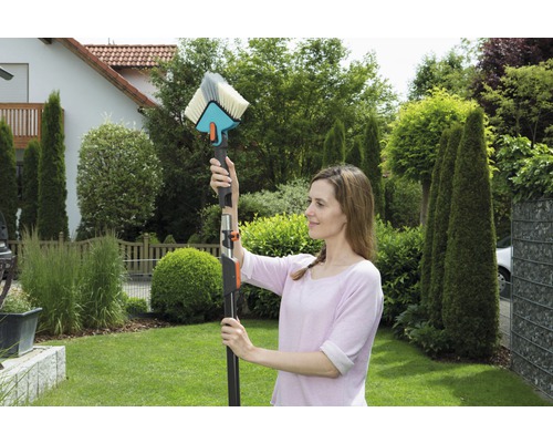 Femeie care folosește o perie de spălat cu tijă telescopică pentru curățenie în grădină.