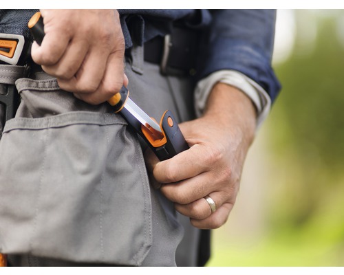 Prim-plan cu o persoană care introduce un cuțit Fiskars în geanta de scule