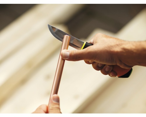 Un bărbat curăță o țeavă de cupru cu un cuțit.